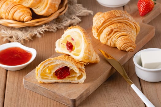 Freshly baked croissants with butter, strawberry jam and tea for breakfast.