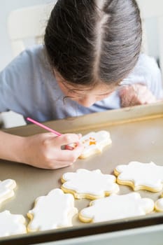 A heartwarming scene of a little girl carefully writing 'Sorry' on sugar cookies with food coloring, the cookies beautifully flooded with white royal icing.