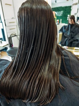 In the bustling atmosphere of a salon, a little girl sits patiently as a stylist with polished red nails carefully trims her damp hair. The sheen of the scissors and the precise hand movements capture the delicate process of styling a child's hair.