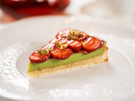 Pistachio cake decorated with strawberries. Crispy tart crust with Pistachio filled layer, decorated fresh strawberry. Portion of perfect pistachio tart on restaurant table