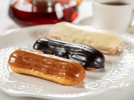 Group of french dessert Eclair on white plate. Caramel, chocolate and vanilla glazed eclairs on white plate in restaurant table background. Perfect french eclairs set