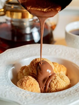Melted chocolate pours onto profiteroles. Profiteroles pouring hot melted chocolate. Effuse chocolate on Profiteroles on restaurant table