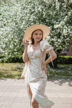 An attractive long-haired woman walks in the spring in the park of blooming apple trees. Spring portrait of a woman