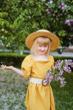 A little girl in a yellow dress and straw hat wearing a bouquet of lilacs. A walk in a spring park, blossoming lilacs