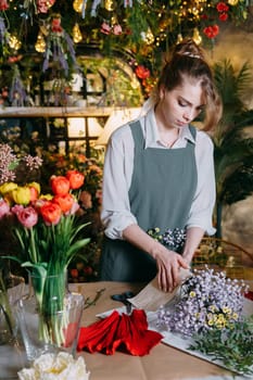 A woman in her florist shop collects bouquets of flowers. The concept of a small business. Bouquets of tulips for the holiday on March 8