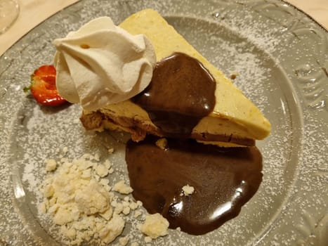 Luscious slice of cheesecake drizzled with rich chocolate sauce, adorned with a fresh strawberry and whipped cream