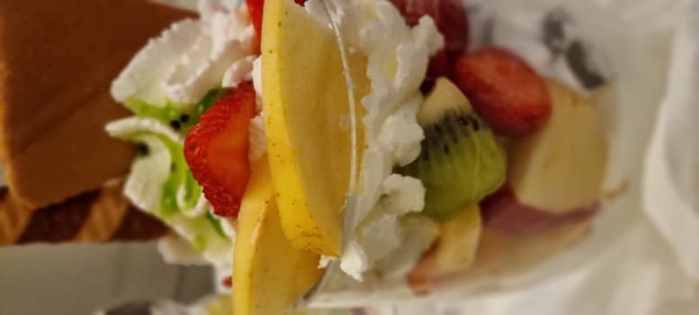 Close-up of a colorful and indulgent fresh fruit parfait with whipped cream, strawberries, kiwi, and waffle cone, making it a healthy dessert option