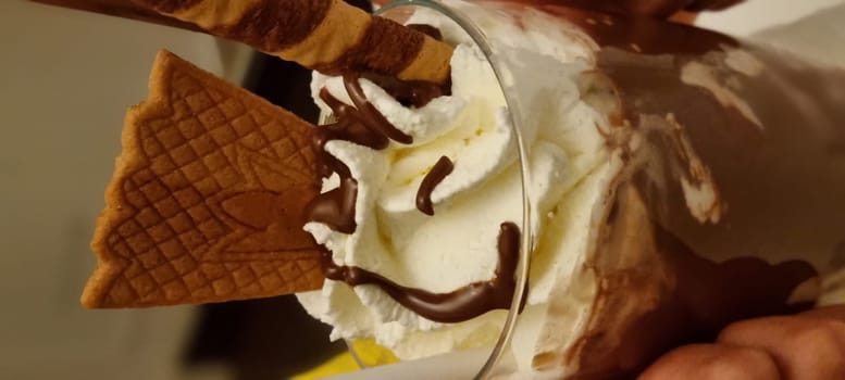 Close-up of a creamy ice cream sundae topped with chocolate drizzle and a waffle cone