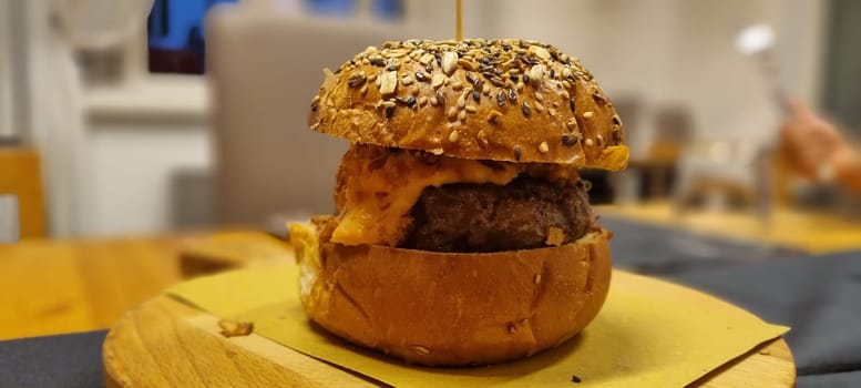 Close-up of a juicy cheeseburger with sesame bun on a wooden table