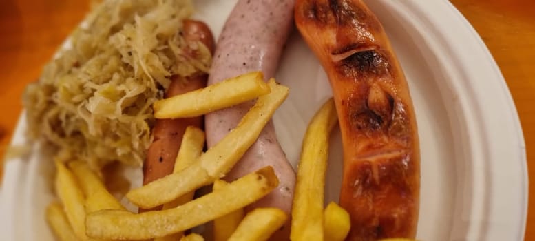 Delicious serving of bratwurst with sauerkraut and fries on a white plate