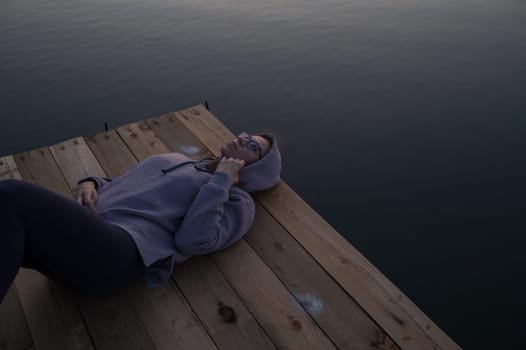 Woman lying down on the pier at lake, closeup portrait, summer sunset