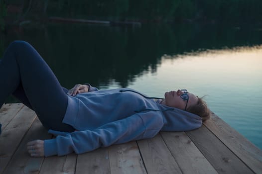 Woman lying down on the pier at lake, closeup portrait, summer sunset