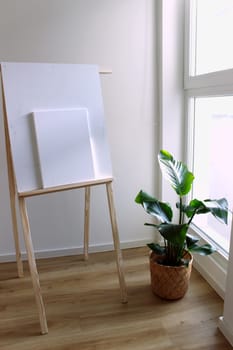 Near the large window is an easel with a canvas for drawing and a houseplant. High quality photo