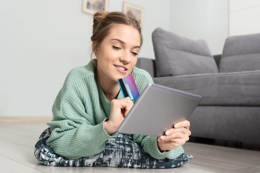 Woman shopping online with tablet. Young person with credit card lying on the floor