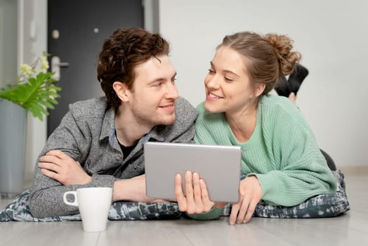 Happy couple with tablet shopping online. Two person lying on the floor, lifestyle concept