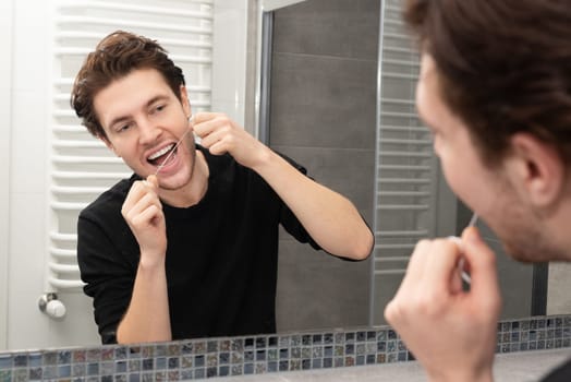 Man using dental floss in bathroom. Dental health concept.