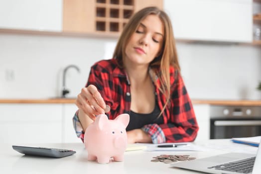 Woman putting money into piggy bank at table. Home budget concept