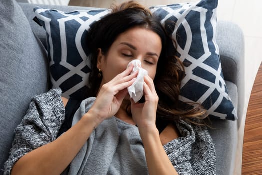 Sick woman blows her nose into a handkerchief, lying on bed