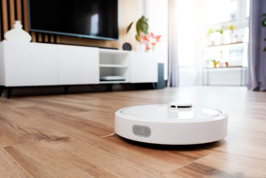 White robot vaccum cleaner on the floor in the living room, smart home device