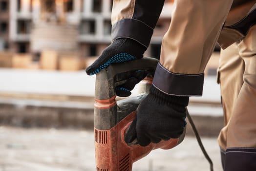 The builder with hammer drill perforator equipment at construction site background.