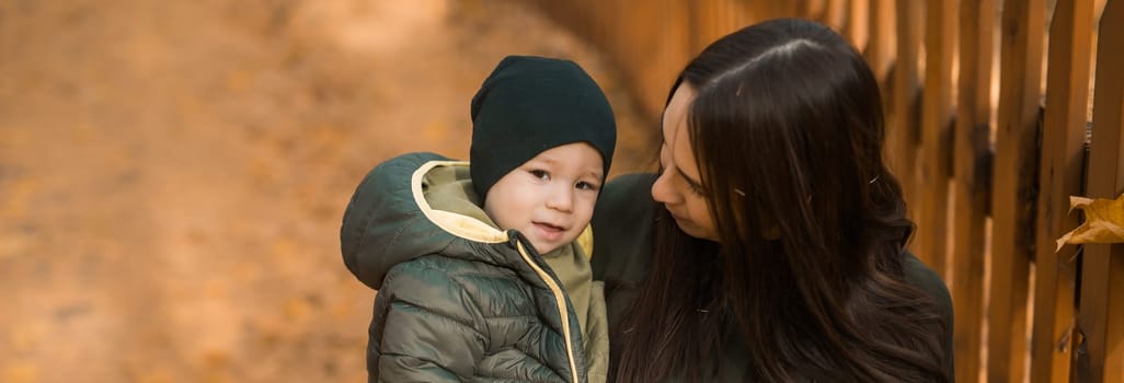 Cute little boy stands with mother outdoors. Happy child walking in autumn park. Toddler baby boy wears trendy jacket and hat. Autumn fashion. Stylish child outside