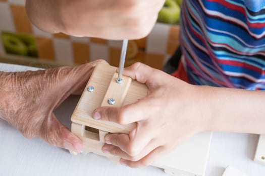 A five-year-old boy independently assembles a wooden construction kit with a screwdriver. Hands close-up