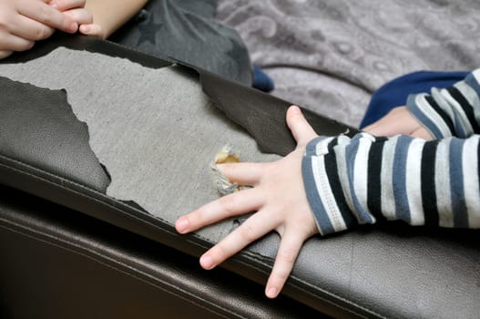 Children's games cause damage to home furniture. A child's finger pierces the sofa and makes a hole in it. Upbringing.