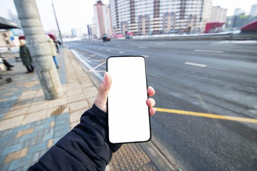 Phone with white screen in hand on city background close up