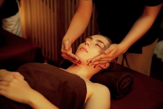 Caucasian woman enjoying relaxing anti-stress head massage and pampering facial beauty skin recreation leisure in warm candle lighting ambient salon spa in luxury resort or hotel. Quiescent