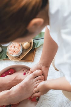 Woman indulges in blissful foot massage at luxurious spa salon while masseur give reflexology therapy in gentle day light ambiance resort or hotel foot spa. Quiescent