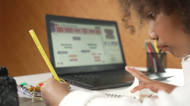 African girl writing car model structure while laptop display code. Smart student working by using laptop develop program or learning programing engineering prompt Erudition in STEM class work.