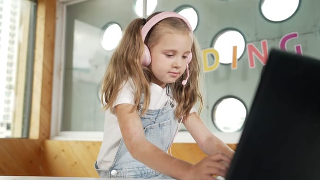 Young student working on laptop or studying in online classroom. Caucasian girl typing on laptop while doing homework or listening music.Little kid wearing headphone. Creative learning. Erudition.