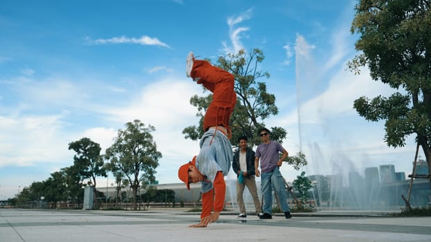 Asian skilled hipster doing freeze pose at camera surrounded by break dancer team near fountain with sky background. Group of handsome people practice b-boy dance. Outdoor sport 2024. Sprightly.