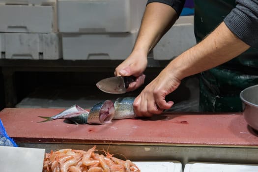 Closeup of male worker's hands cutting fish with knife at table.