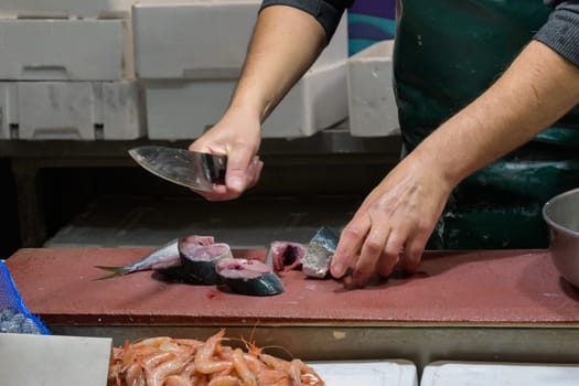 Closeup of male worker's hands cutting fish with knife at table.