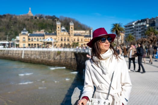 Stylish woman with maroon hat and white coat on Paseo de la Concha, San Sebastian