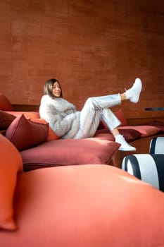 Model with white fur coat on red sofa, Spain