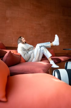 Model with white fur coat on red sofa, Spain