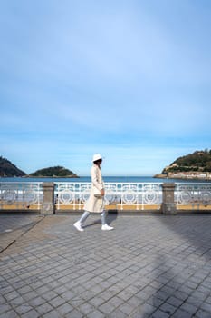 Stylish woman with white coat and hat on Paseo de la Concha, San Sebastian