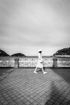 Stylish woman with white coat and hat on Paseo de la Concha, San Sebastian