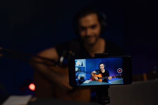 Host channel of smart influencer in creative audio with clearly smartphone live streaming with blur background, sing with play guitar music blogger social media online at neon light studio. Surmise.