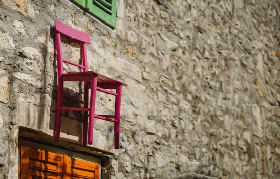 Funny pink wooden chair nailed to old stone wall of house, Biograd na Moru in Croatia