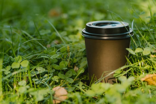 Hot drink in disposable paper cup for coffee break in park, mug on green grass