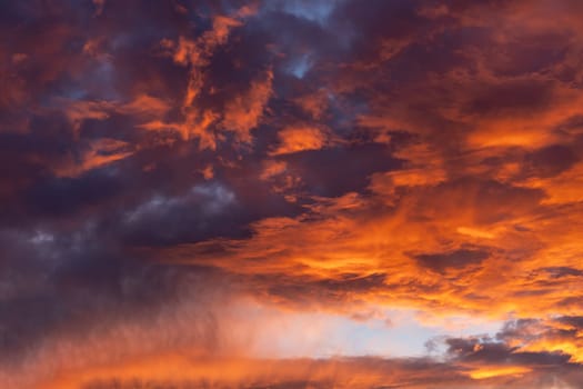 Dramatic fiery cloudy evening sky at sunset, clouds of bright colors in twilight