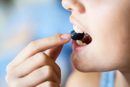Closeup of unrecognizable crop teenage girl biting fresh organic blueberry at home