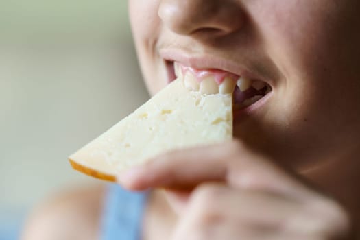 Closeup of crop happy unrecognizable teenage girl biting fresh cheese slice at home