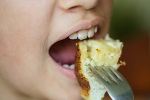 Closeup of crop anonymous young girl eating delicious potato omelette from fork at home