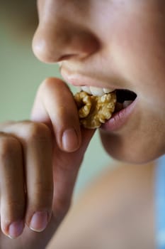 Closeup of crop anonymous young girl eating healthy walnut kernel at home