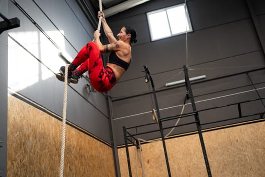 Low angle view photo with copy space of a fit mature woman climbing a rope in a cross training gym