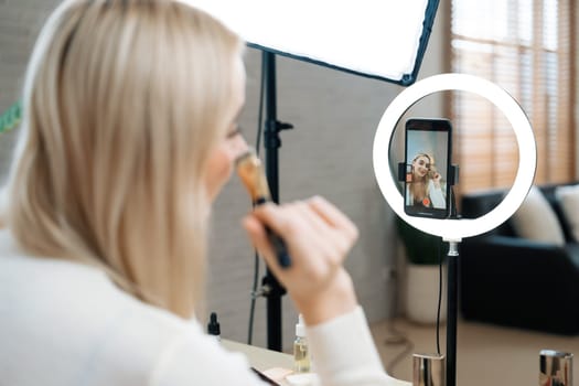 Rear view young woman making beauty and cosmetic tutorial video content for social media. Beauty blogger showing how to apply beauty care to audience or follower on camera screen. Blithe